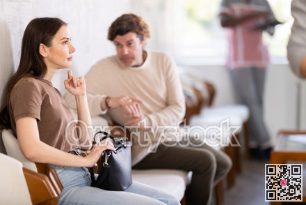 Young woman and middle-aged man talking while sitting in waiting area
