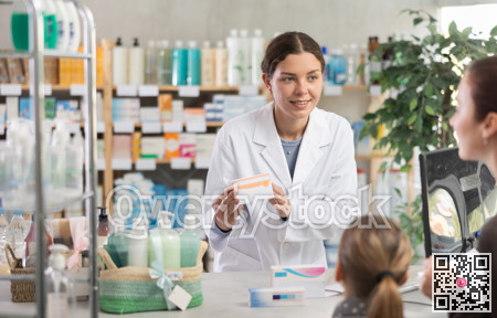 Young female pharmacist offering medicament to mother with daughter in chemistry