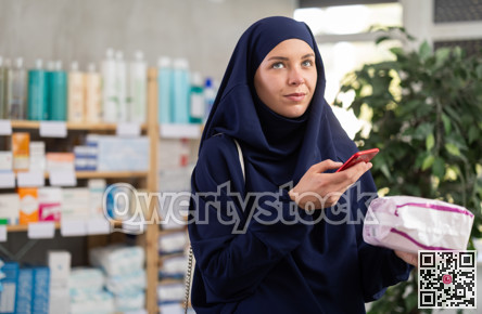 Muslim female shopper scanning barcode to read pad reviews in drugstore