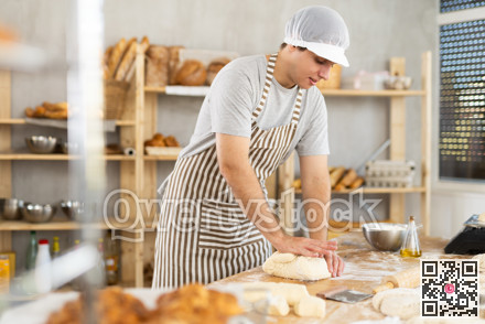 Young man assistant baker in apron training kneading dough in small kitchen at bakery, food and pastry concept