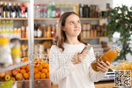 European teen girl customer at shop scans QR code on peach juice bottle using phone camera