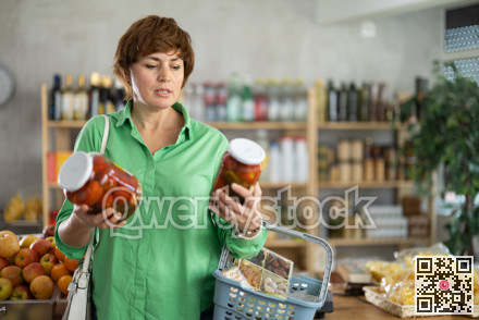 Female shopper selects pickled tomatoes in the produce section of supermarket