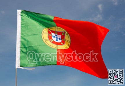 Beautiful large red and green Portuguese flag waving in wind against blue sky.