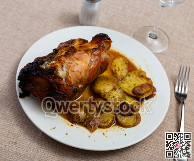 Portion of pork knuckle with boiled potatoes and gravy in plate