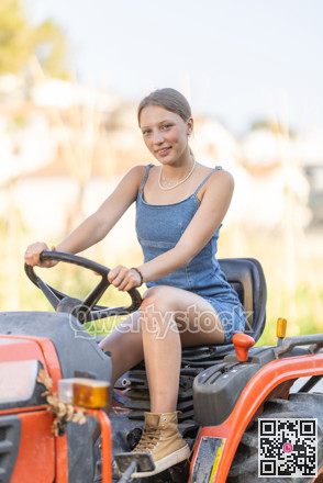 Young woman sits on minitractor and drives rural vehicle, performs loading work on farm