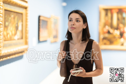 Woman visiting museum and looking at paintings in gold frames