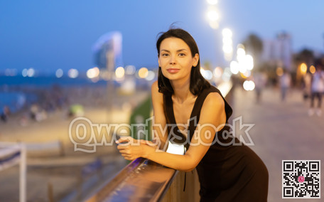 At night, Woman put hands on fencing, watching towards beach of Barceloneta