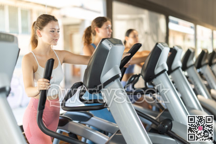 Positive young girl training on elliptical machine in gym