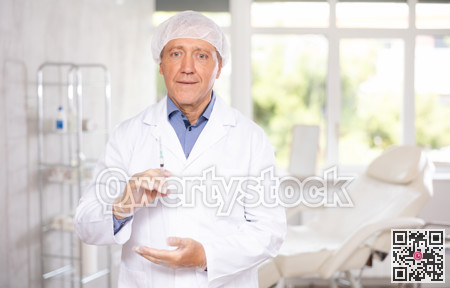 Aged male doctor standing in clinic office with syringe in hands