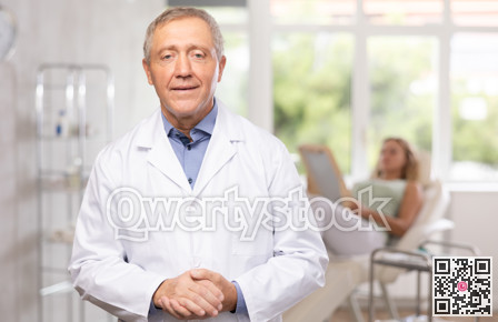 Elderly doctor standing in clinic office with patient lying on couch