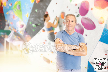 Portrait of positive elderly male coach against background of climbing wall