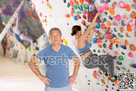 Positive experienced elderly climber standing near bouldering wall