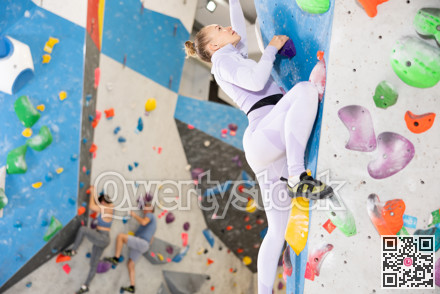 Focused woman climbing without ropes and harnesses on artificial bouldering wall