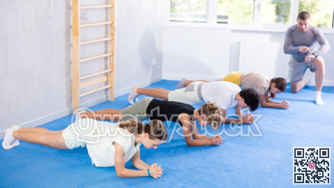 Group of preteen children doing push-ups on sports mats during a self-defense class in gym