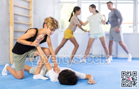 Two preteen boys learn to do power grabs in pairs during a self-defense lesson under the guidance of trainer in the gym