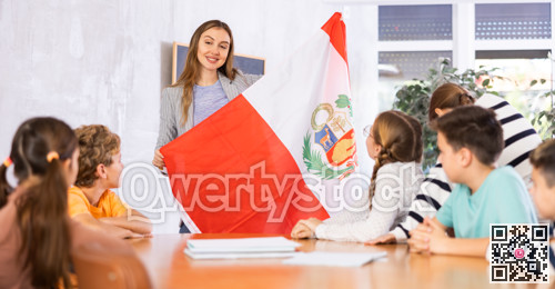 Excited young female teacher showing flag of Peru to schoolchildren preteens during history lesson in classroom