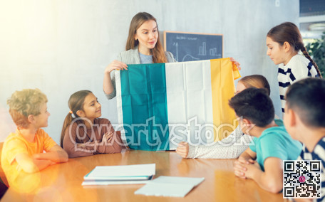 Female teacher tells her classmates about the country of Ireland, holding flag in her hands