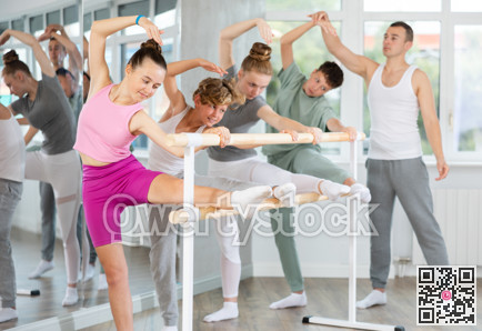 Teenage boys and girls practicing leg stretching exercise during ballet classes