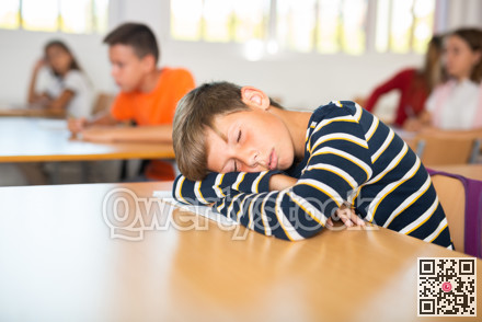 Bored tween schoolboy sleeping at desk in classroom during lesson