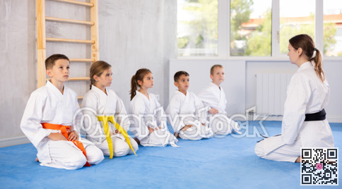 Children in white kimono sitting on knees on tatami in gym