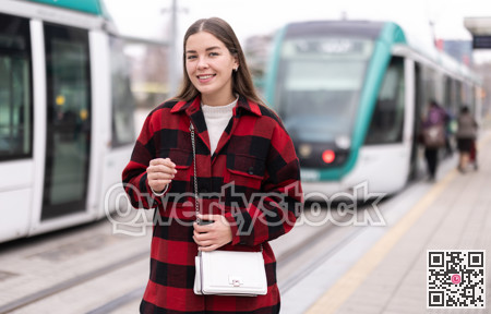 Girl is standing on street platform, waiting for tram to arrive