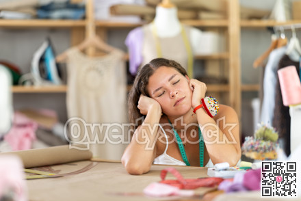 Tired female fashion designer sleeping at worktable in sewing studio