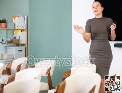 Young woman coach presenting in auditorium with remote control