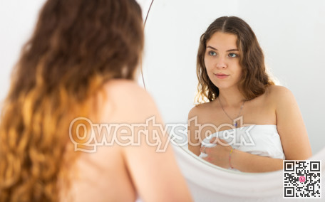 Girl with a towel on her head looks in mirror