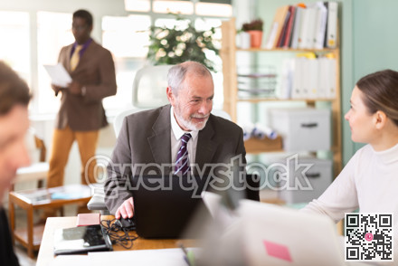 Senior man sitting at desk is working on laptop computer. Working day in office