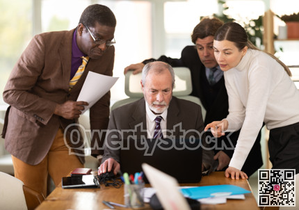 Team businessmen discusses business project while gathered around laptop in company office
