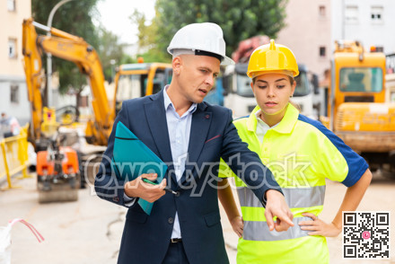 Civil engineer discussing a construction plan with a young woman worker shows her something