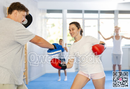 Positive woman in boxing gloves practicing punches on mitts with husband