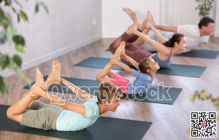 Diligent preteen boy practicing bow pose of yoga with his family