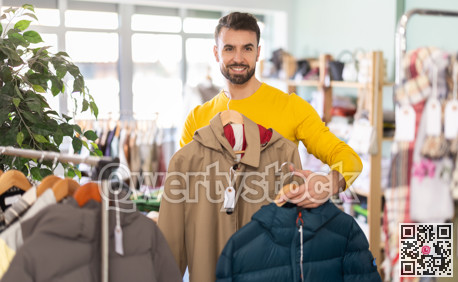Young man choosing down jacket in clothing store