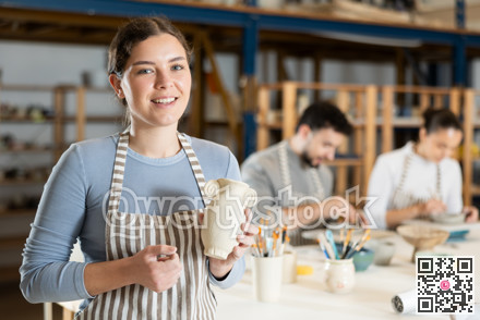 Girl in apron stands with vase in hands, finished clay products from craftsperson