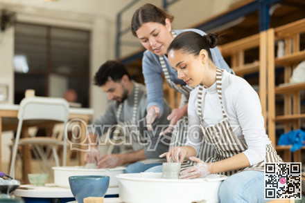 Woman help girl sculpting ceramic product from raw clay on pottery wheel in workshop
