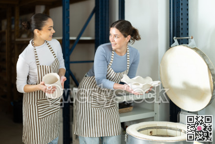 Girl in apron put or takes clay vase out of oven