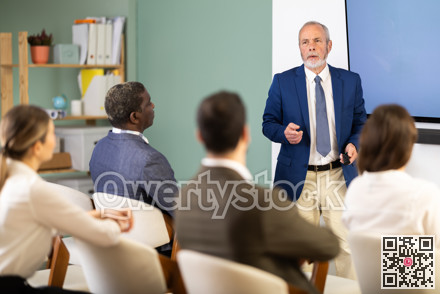 Senior man lecturer with remote controller speaks to business audience of listeners