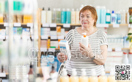 Mature female buyer choosing skin cream at drugstore