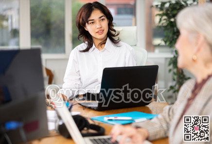 Positive young woman sitting at desk and typing on laptop in office