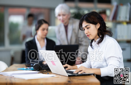 Young woman works on laptop with female colleagues
