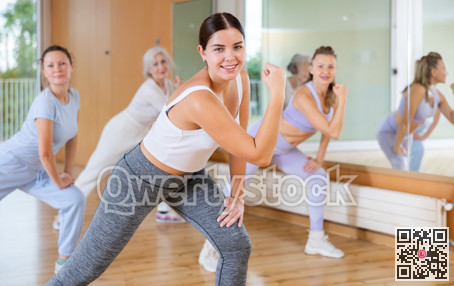 Cheerful energetic women amateur dancers of different ages moving leg to side at lesson with coach in dance hall