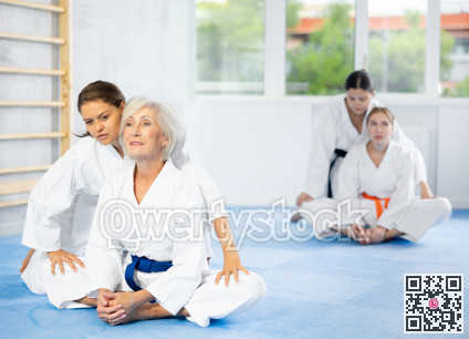 Female trainer helping woman in kimono sit in butterfly pose in gym