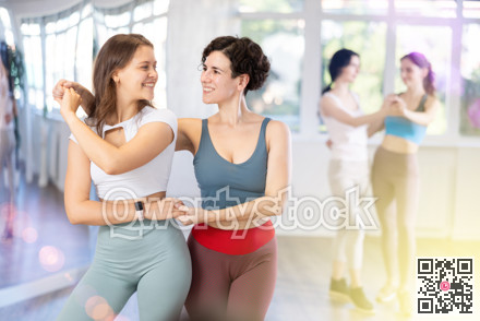 Two cheerful young women dancing bachata as pair in dance studio