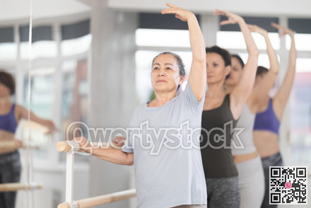 Female amateurs stand in third position near ballet barre during group training in dance studio