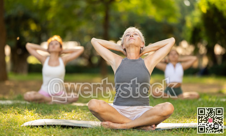 Happy old lady and class of calm sports women in activewear stretching muscles of neck while sitting in lotus pose on mats during yoga training together at city