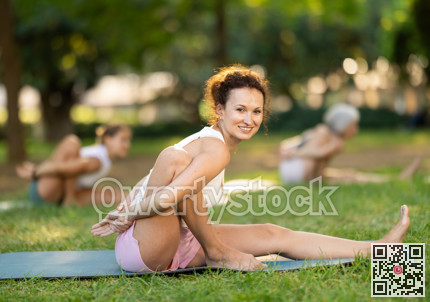 Fit woman performing Marichyasana at group yoga session in park