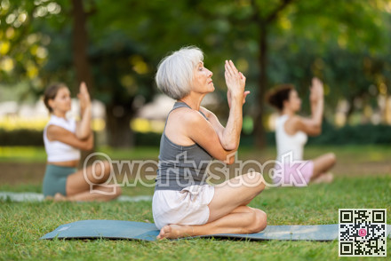 Elderly woman performing Gomukhasana Garudasana during outdoor group yoga training