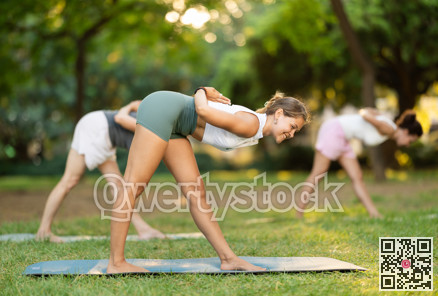 Sportive focused mixed age group of women standing in Parivrtta Trikonasana or Revolved Triangle Pose on mats during group yoga training in green park