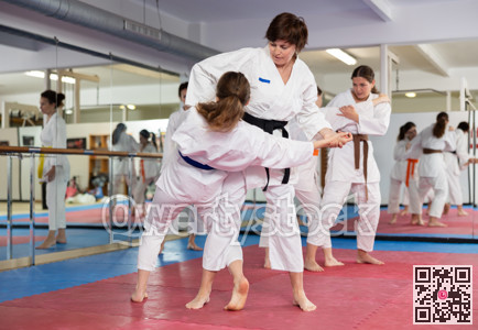 Womens practicing new karate moves in pairs in class with trainer